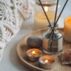 木製のトレイに置かれたアロマディフューザーと、優しく灯る複数のキャンドル。マクラメ編みのクッションが添えられた、ヒュッゲでリラックスした空間の演出。