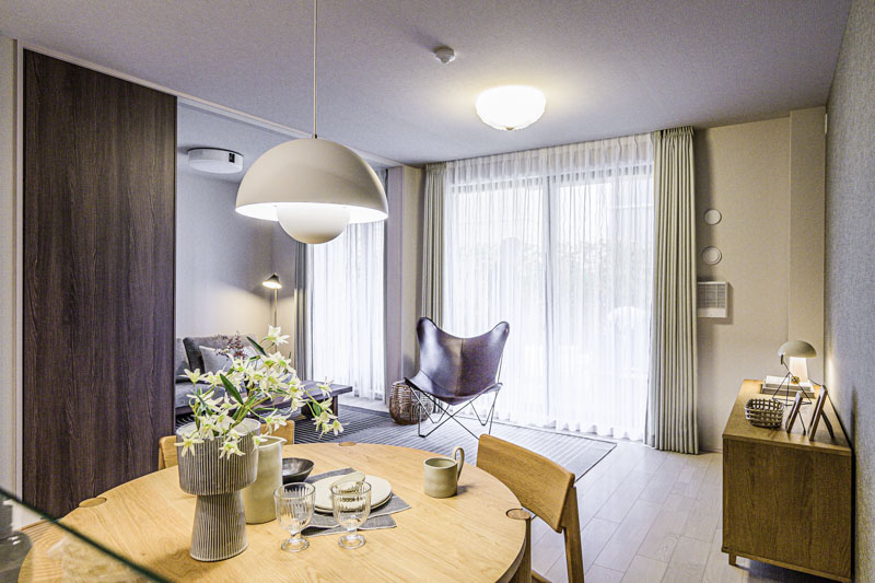 温かみのある間接照明に照らされた、整然と片付いたリビングダイニング。丸いダイニングテーブルの上には花が飾られ、奥にはバタフライチェアが配置された、心が安らぐ上質なインテリア空間。